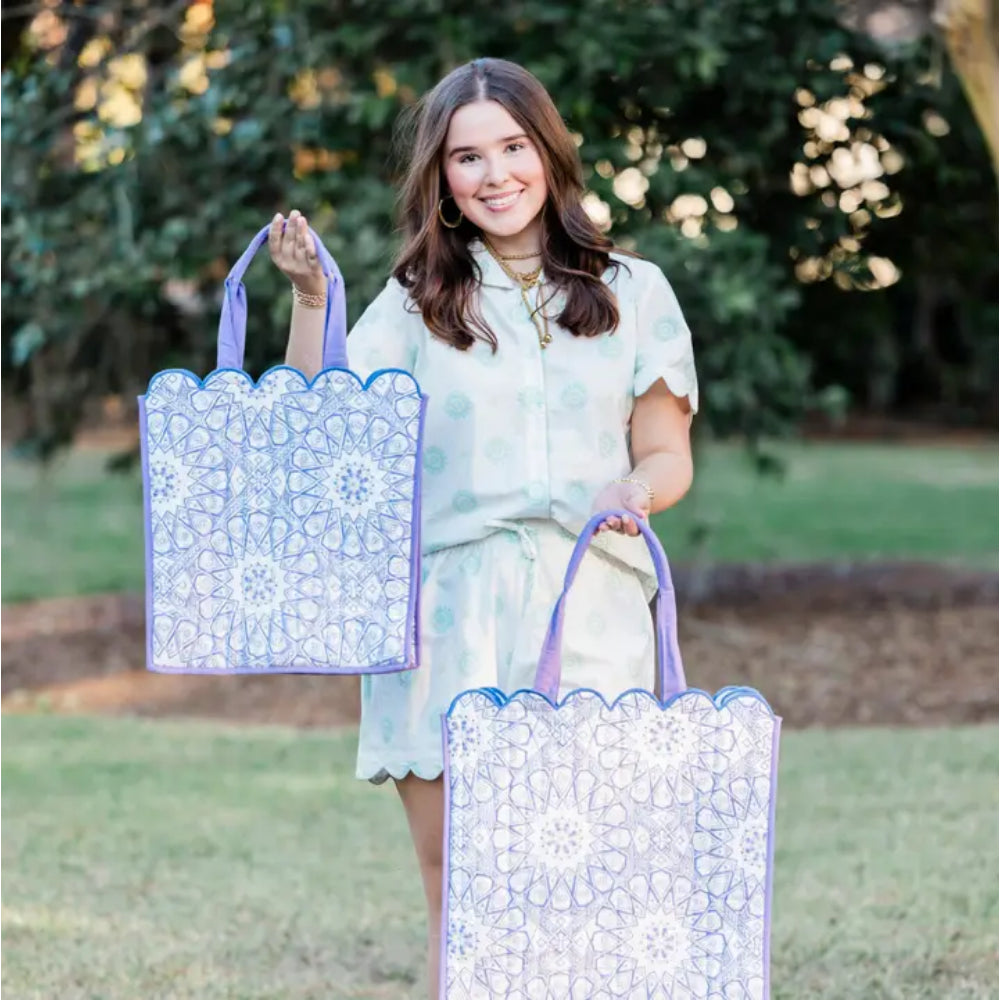 Woman holding two patterned totes outdoors with greenery in the background