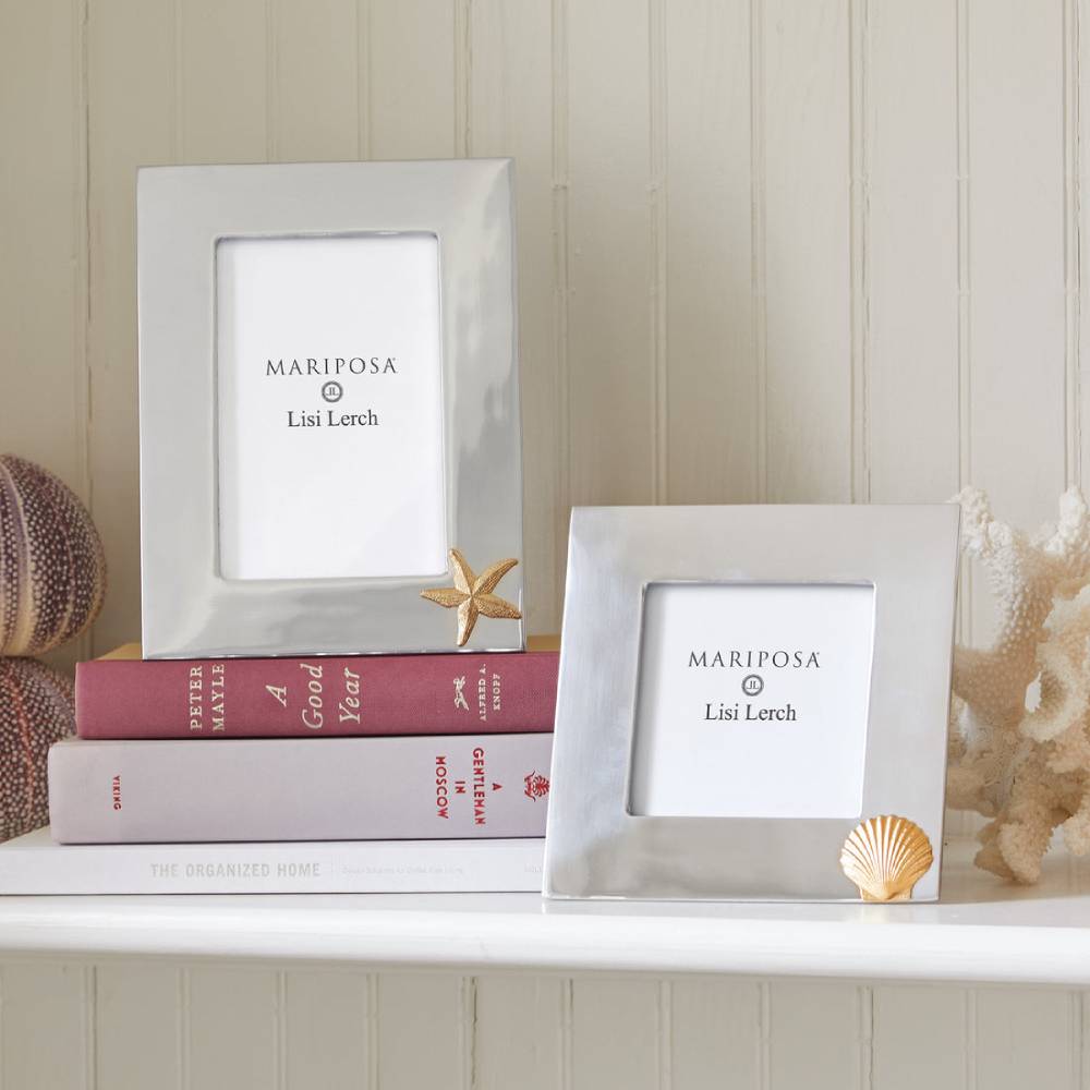 Two silver picture frames with 'Mariposa' branding on a shelf with books and decorative items.