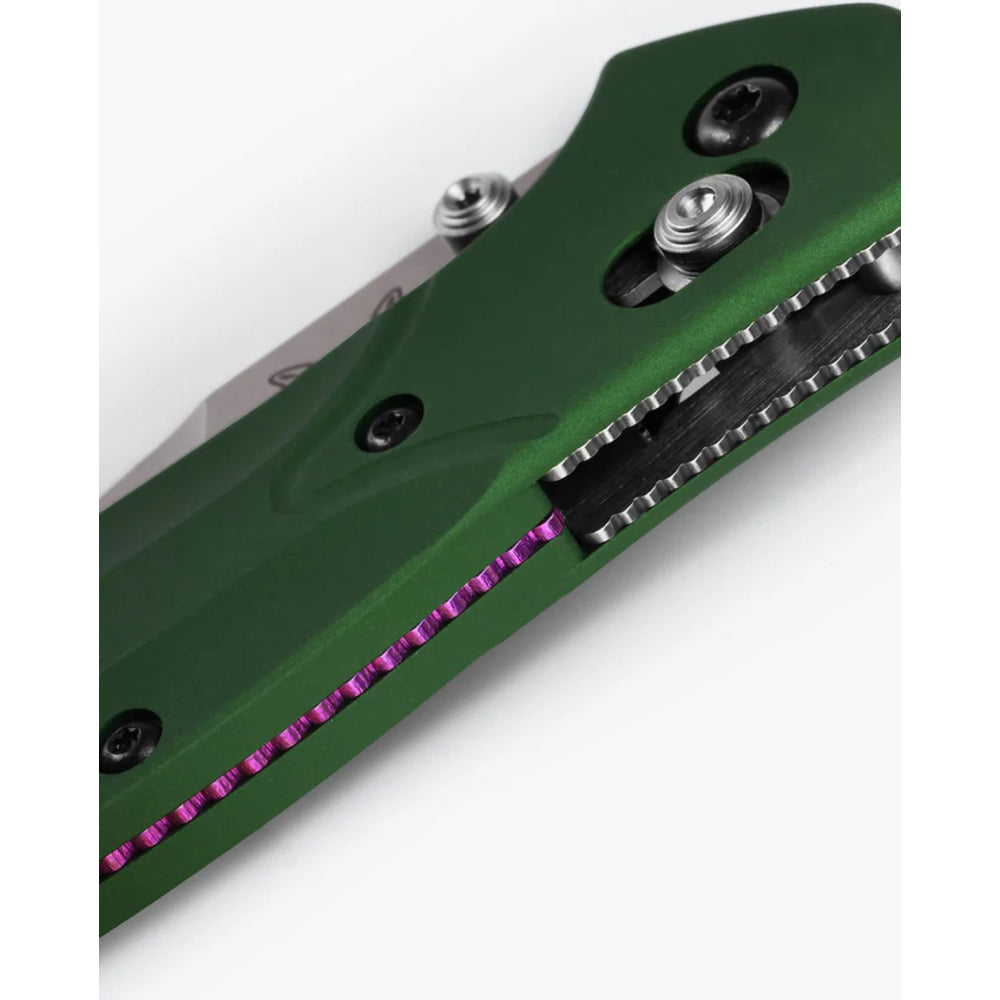 Close-up of a folding knife handle in matte green with a purple accent line and silver hardware, shown on a white background.
