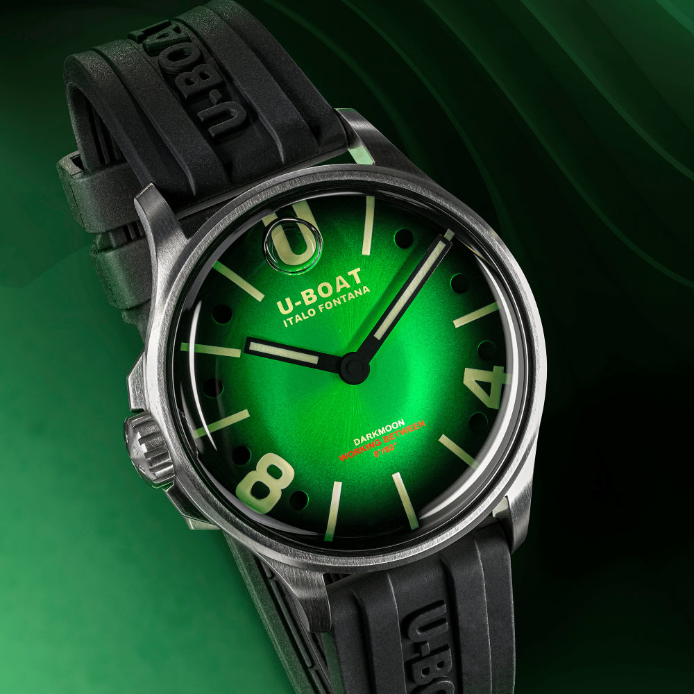 A close-up of a U-Boat hand-forged watch with a bright green dial, green Arabic numerals, and a black rubber strap with 'U-BOAT' embossed on it, set against a dark green background.