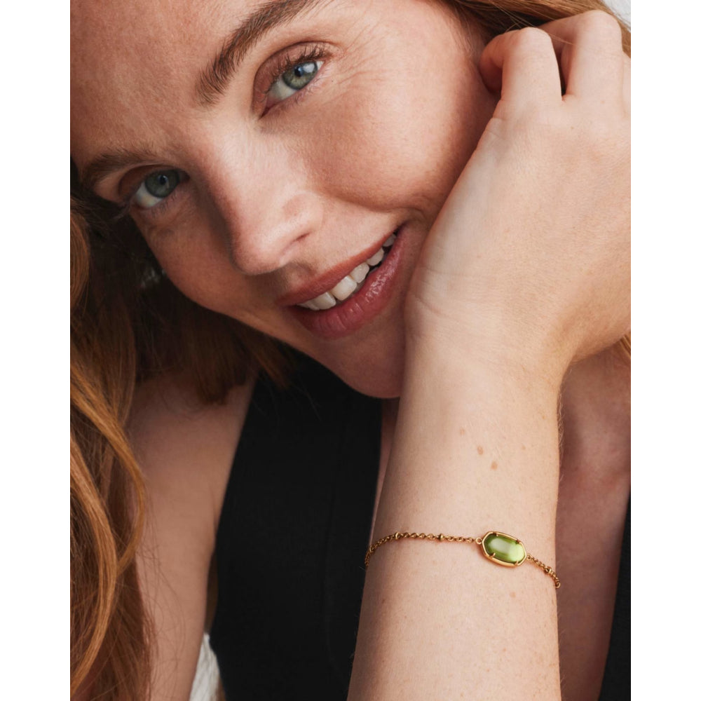 A close-up lifestyle shot of a woman wearing a delicate gold chain bracelet with a small, polished olive-green stone on the wrist.
