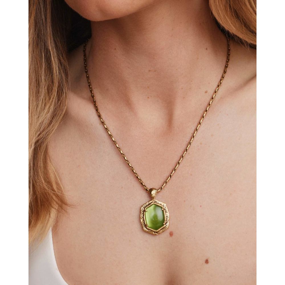 A gold chain necklace with a hexagonal green gemstone pendant, shown worn on a model's neck.
