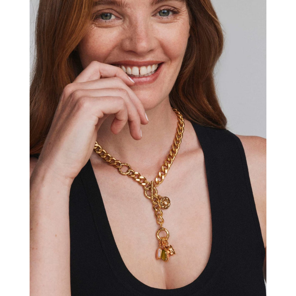 A woman with red hair wearing a chunky gold chain necklace with a dangling gold elephant charm, paired with a black tank top.