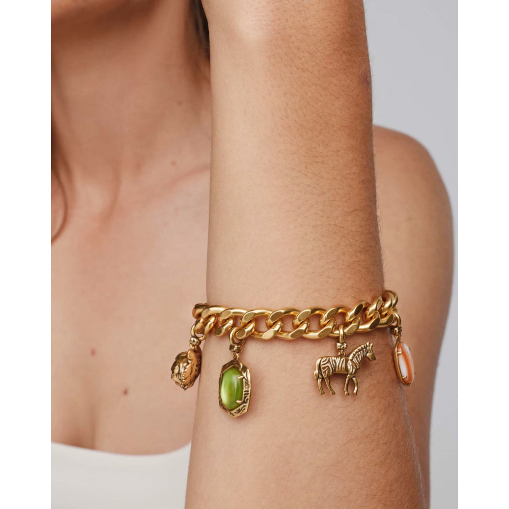 A gold chain bracelet with multiple charms, including a horse, a green oval stone, and a small orange pendant, worn on a model's wrist.