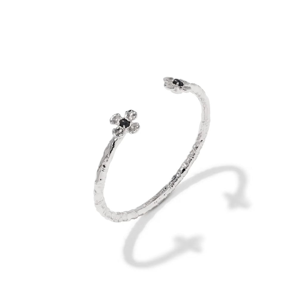A silver textured open cuff bracelet featuring a small flower motif with black and clear stones on one end, displayed on a clean white background with a soft shadow.