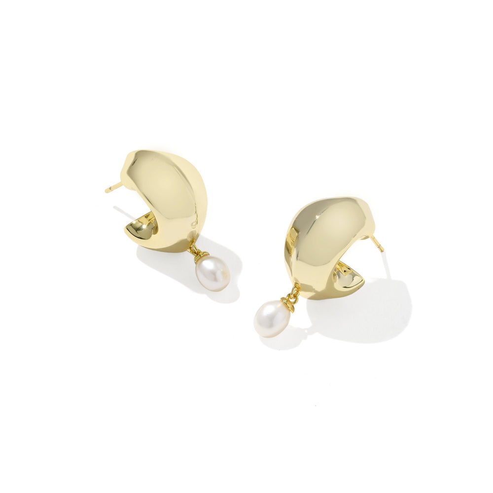 A pair of gold huggie hoop earrings with a dangling white pearl, shown on a clean white background with soft shadows.