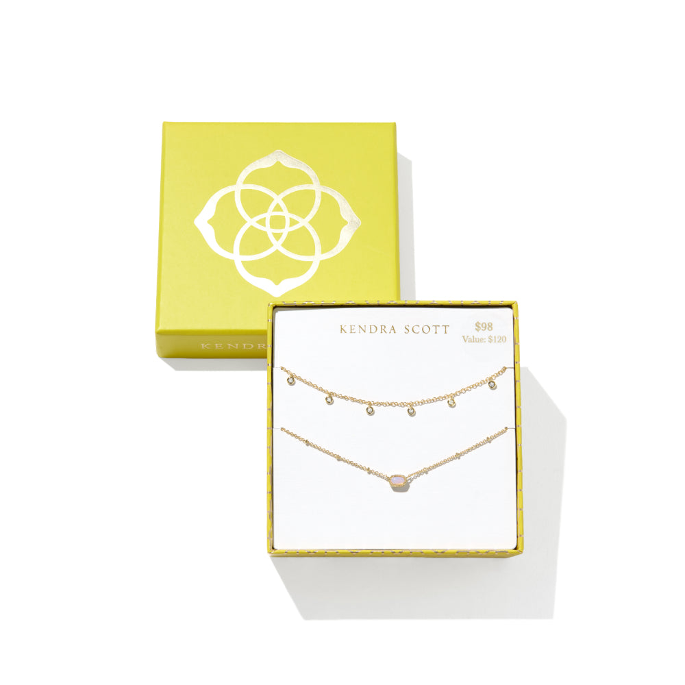 A gold double-strand necklace set by Kendra Scott, displayed in its white and gold presentation box next to its lime green brand box on a white background.