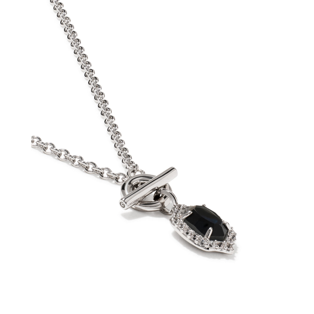 A silver-toned necklace featuring a toggle clasp and a teardrop-shaped pendant with a central black gemstone surrounded by small clear stones, set against a plain white background.