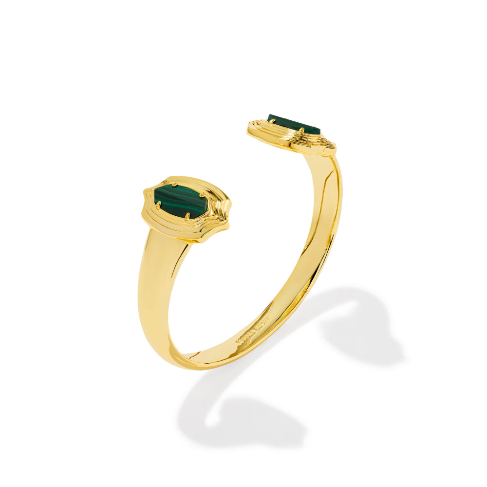 A gold open cuff ring featuring two emerald-cut green gemstones, displayed on a clean white background with a soft shadow.