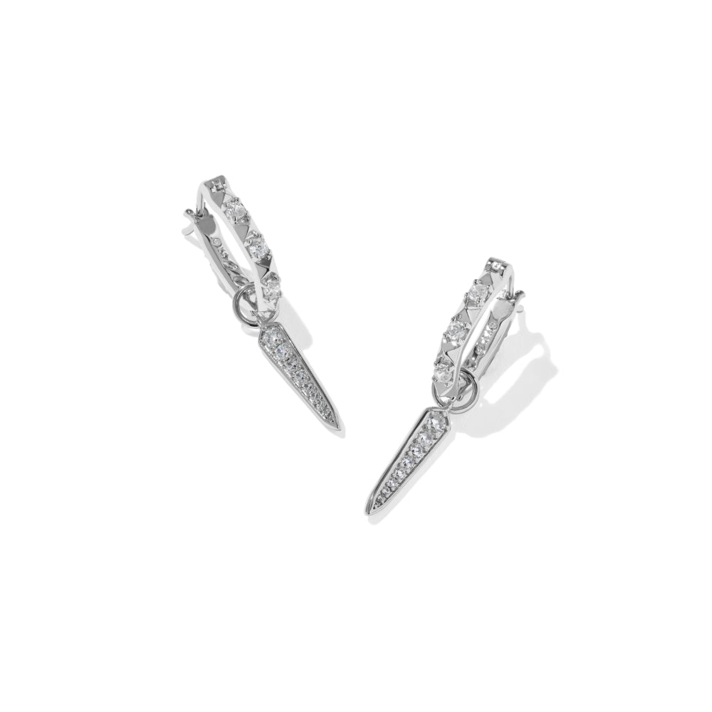 A pair of silver-toned huggie hoop earrings with dangling spear-shaped drops, both adorned with pavé-set clear stones, shown on a clean white background.