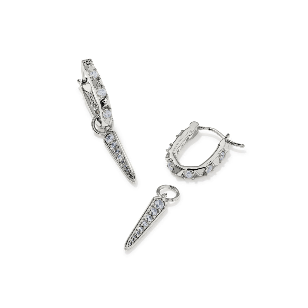 A pair of silver-toned huggie hoop earrings with elongated spike charms, both adorned with small clear pavé stones, shown on a clean white background.