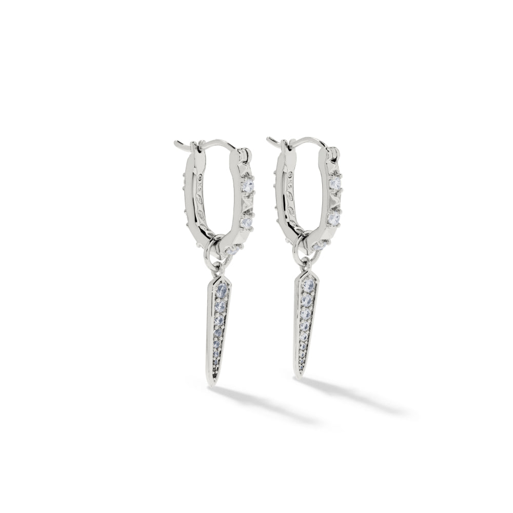 A pair of silver hoop earrings with small clear stones along the outer edges and a dangling pointed spike charm paved with clear stones, shown on a white background.