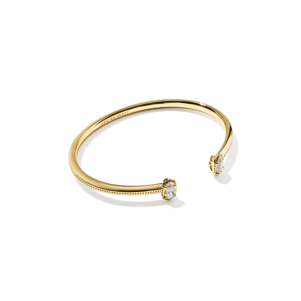 A gold open cuff bracelet with two small clear gemstone settings, shown on a clean white background.