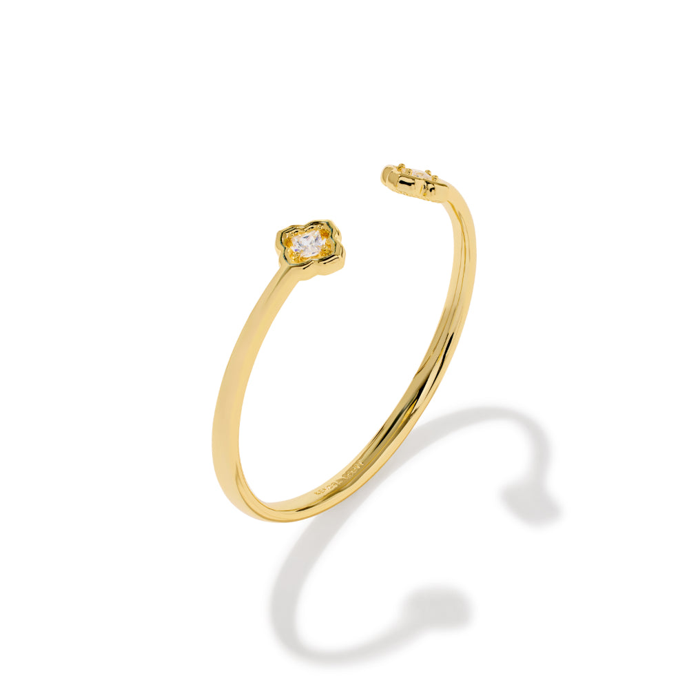 A polished yellow gold open cuff bracelet featuring a small, bezel-set clear gemstone at the top, shown on a clean white background with a soft shadow.
