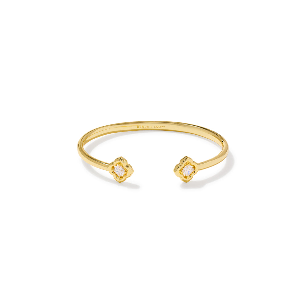 A gold open cuff bracelet with two small diamond-like stone settings on the ends, shown on a clean white background. The inside of the band is engraved with the brand name 'SARABY'.