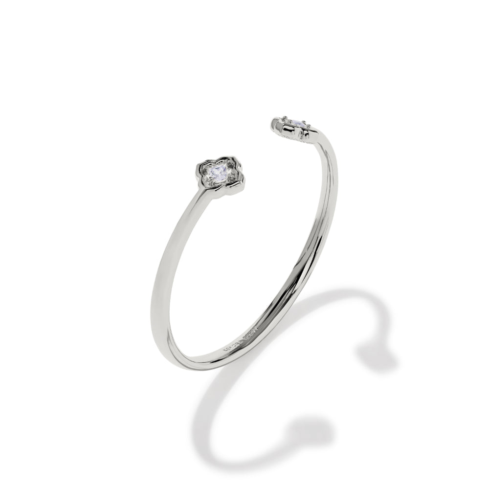 A polished silver-toned open cuff bracelet with a single bezel-set clear gemstone on a plain white background.