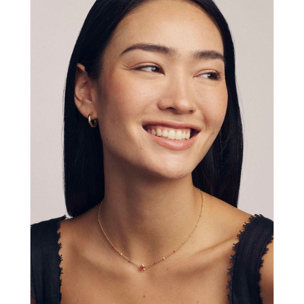Woman wearing a necklace with a red pendant against a plain background