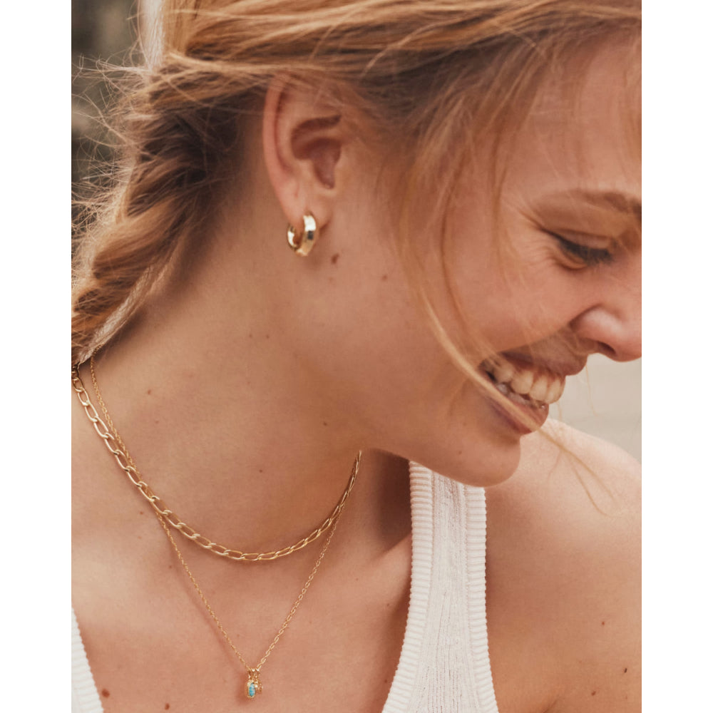 Woman wearing gold jewelry including a necklace and hoop earrings.