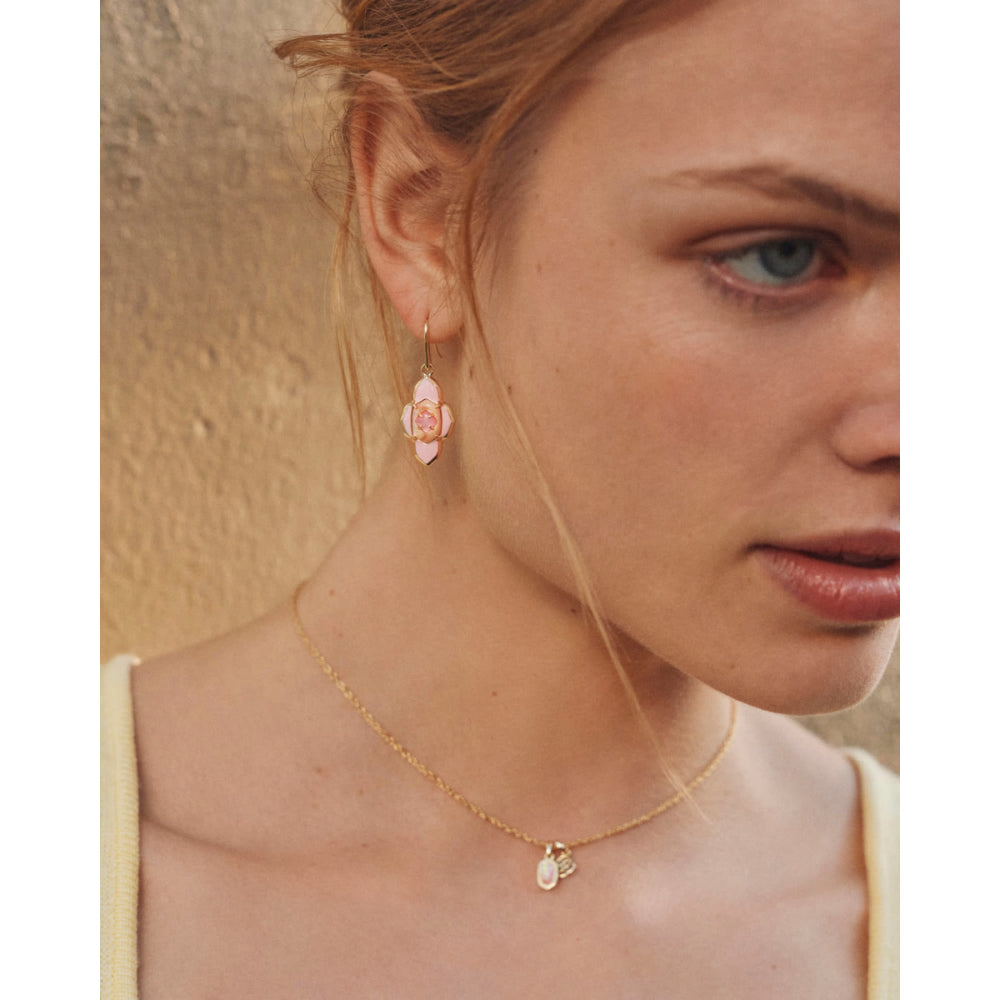 Close-up of a woman wearing a gold necklace and pink earrings against a neutral background