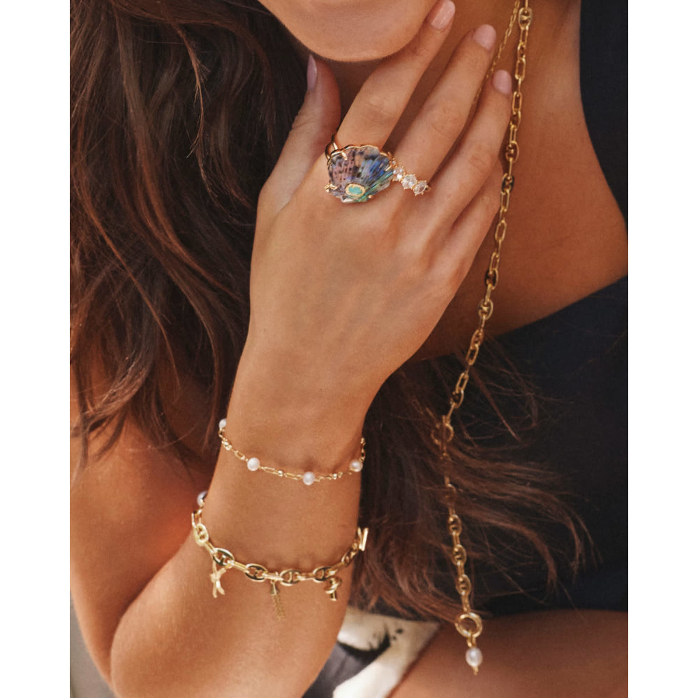 Close-up of a hand wearing a gold ring, bracelet, and necklace with a multicolored gemstone.