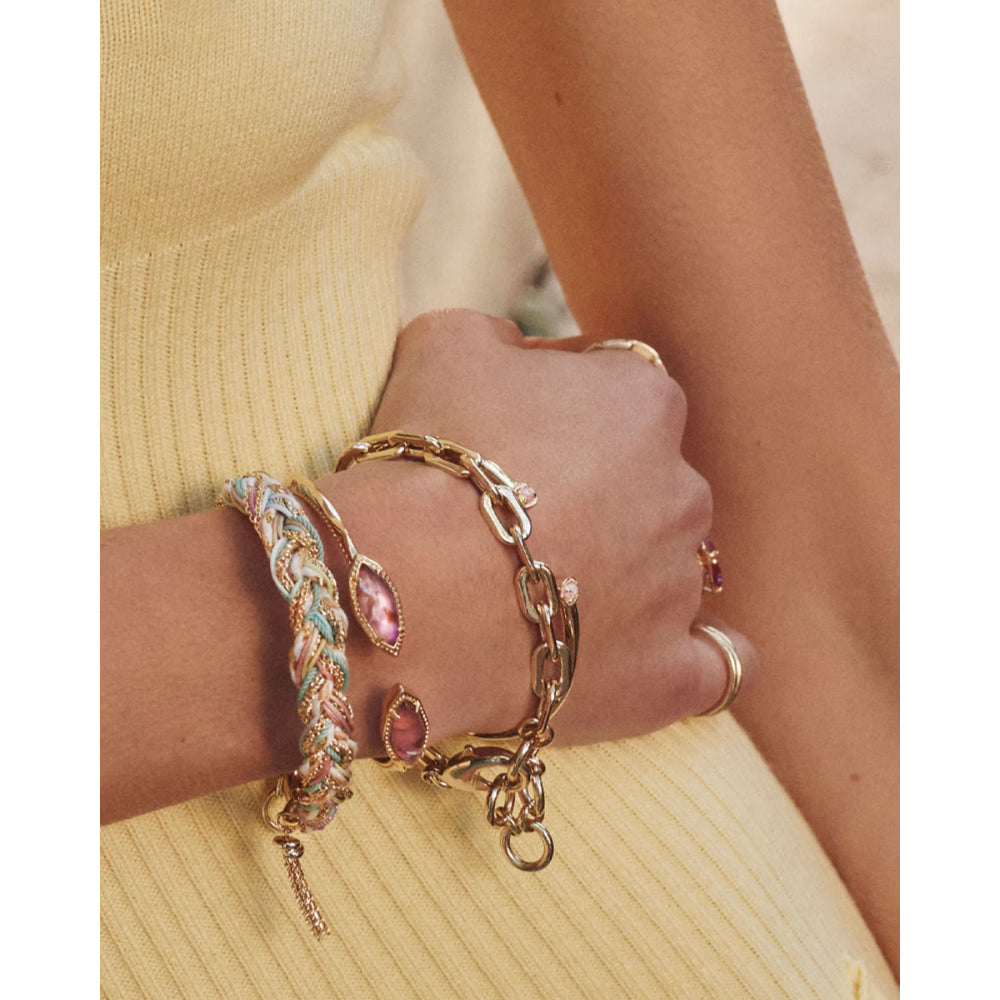 Close-up of a hand wearing multiple gold bracelets with gemstones on a neutral background