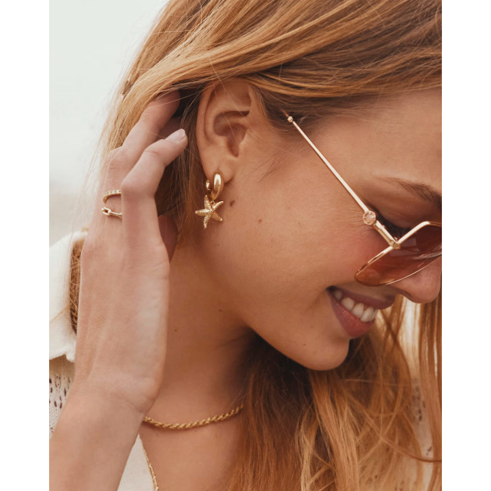 Close-up of a woman wearing gold earrings and sunglasses with a blurred background