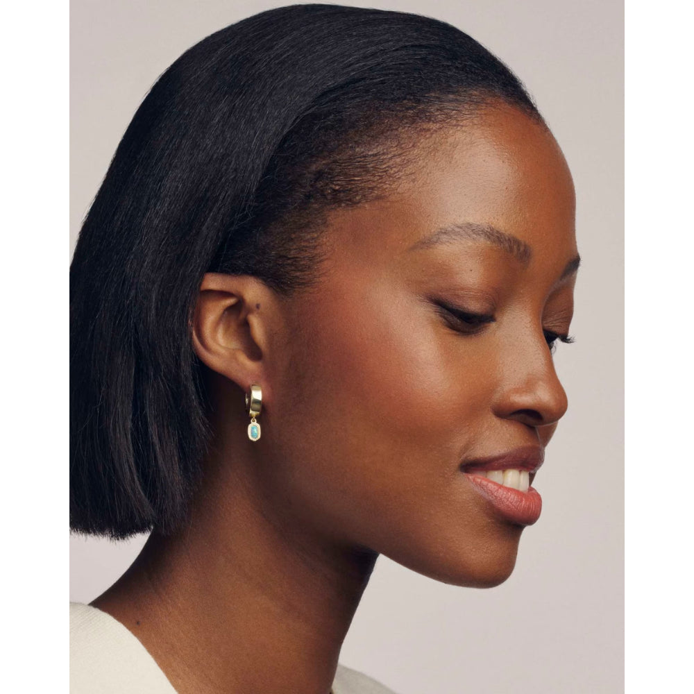 Woman with a short black bob hairstyle wearing gold earrings against a plain background