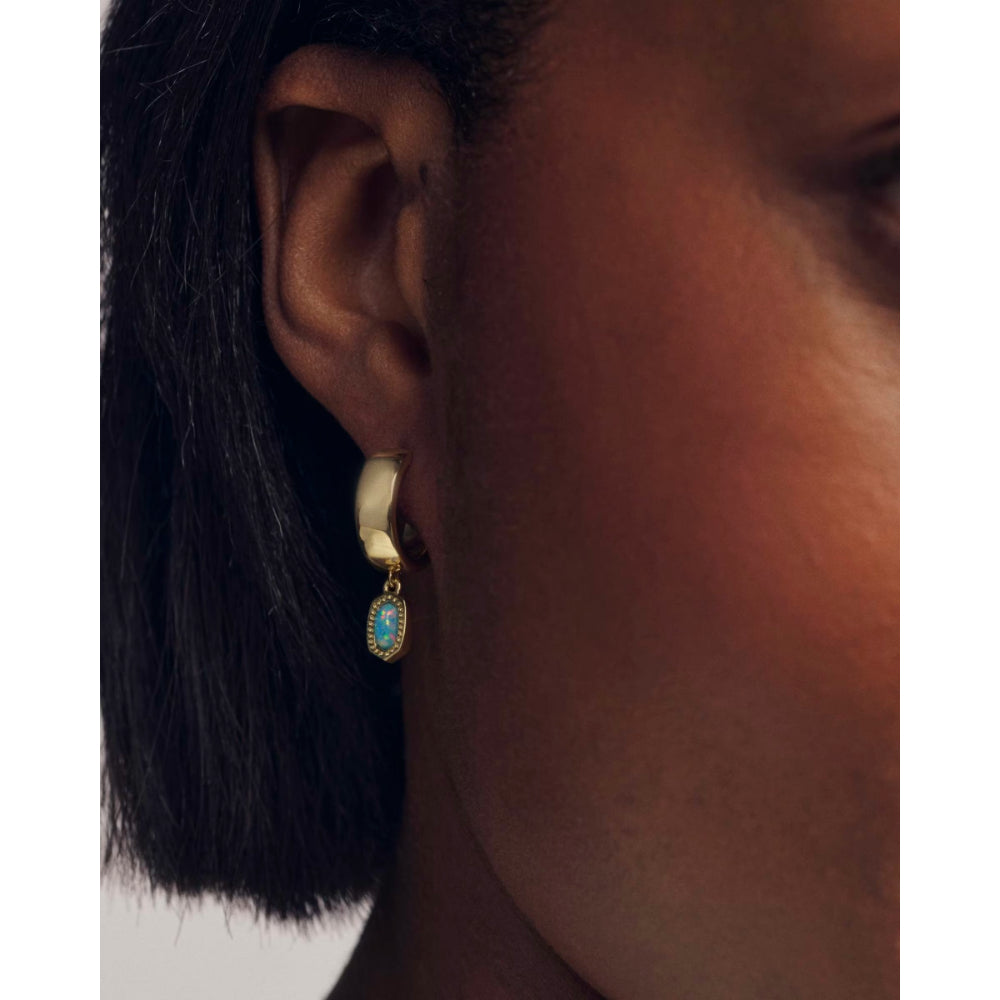 Close-up of an ear wearing a gold earring with a blue gemstone on a white background