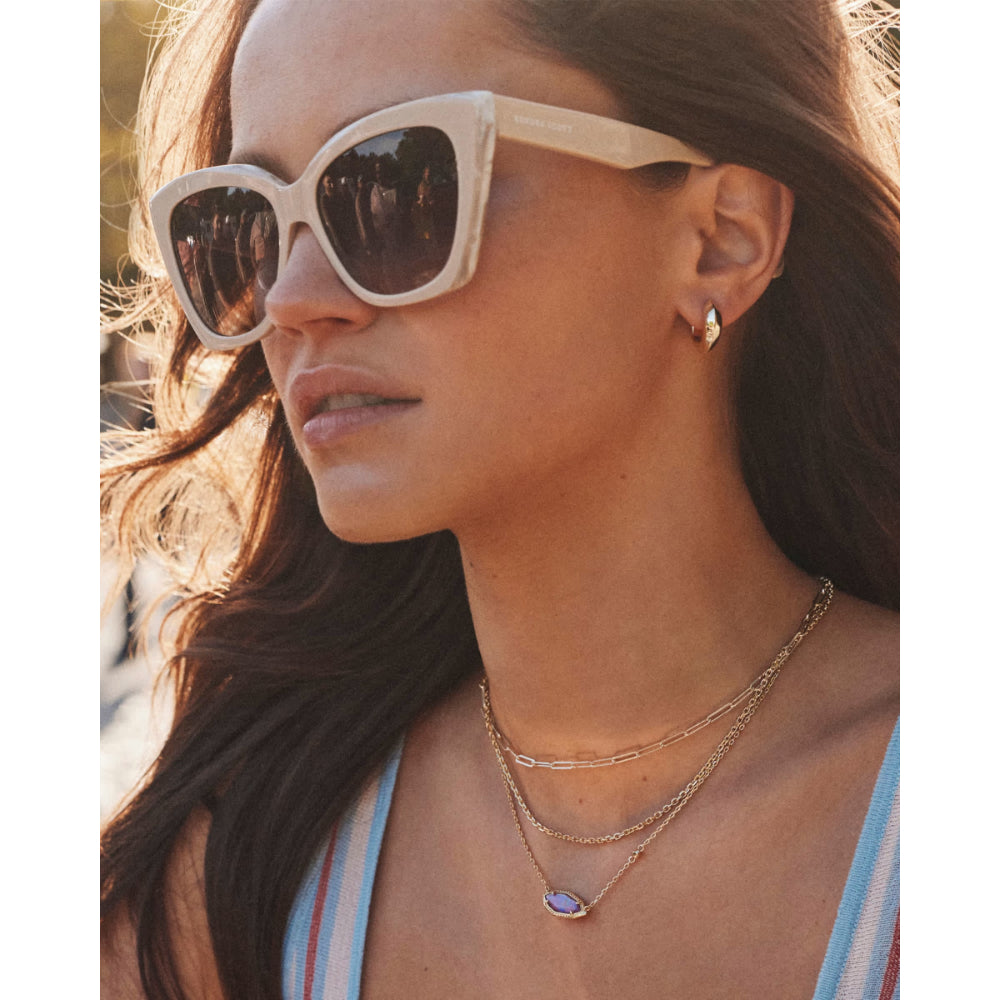 Woman wearing sunglasses and layered necklaces with a blurred background
