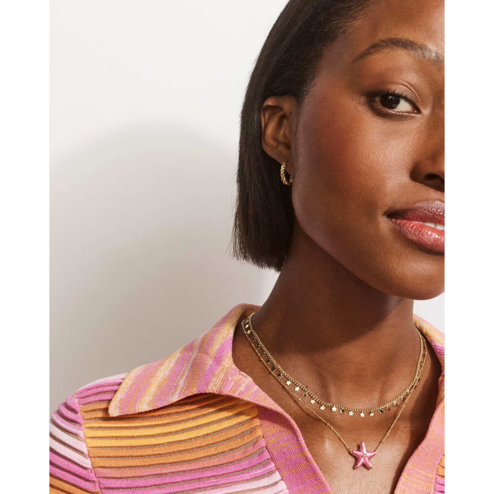 Woman wearing a pink and orange striped shirt with a gold necklace featuring a star pendant.