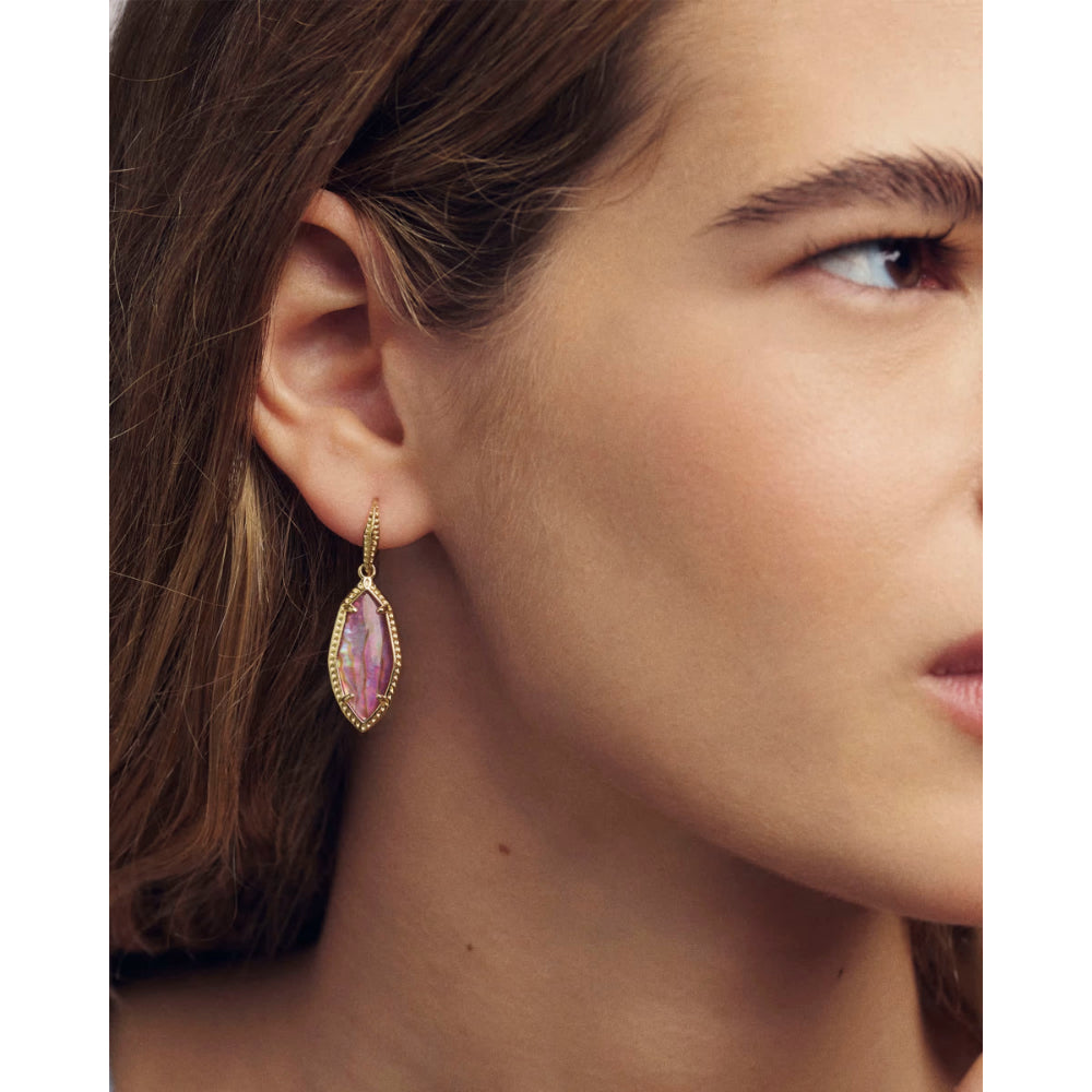 Close-up of a woman wearing a gold earring with a pink gemstone.