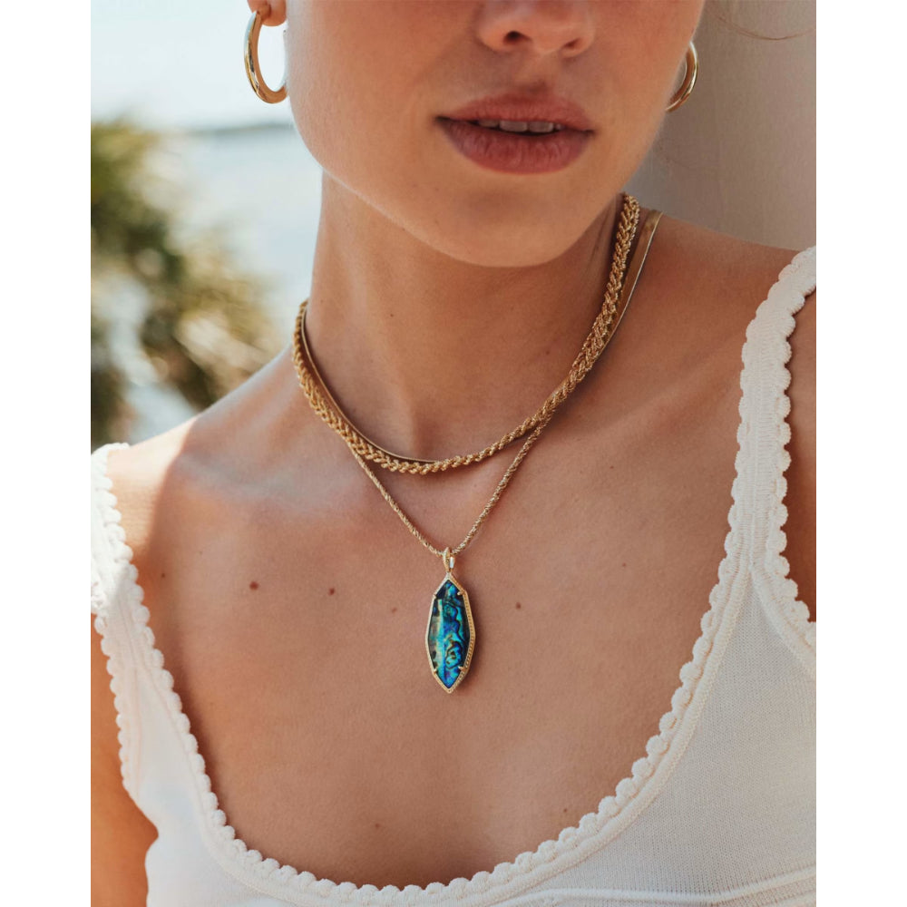 Close-up of a person wearing a gold necklace with a blue pendant, outdoors.