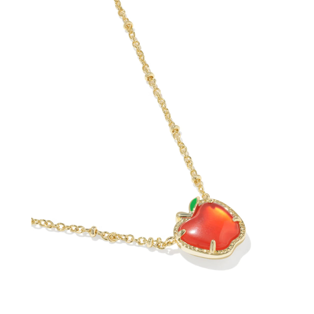 A gold necklace featuring an apple-shaped pendant with a translucent red-orange cabochon and a small green leaf accent, set against a plain white background.