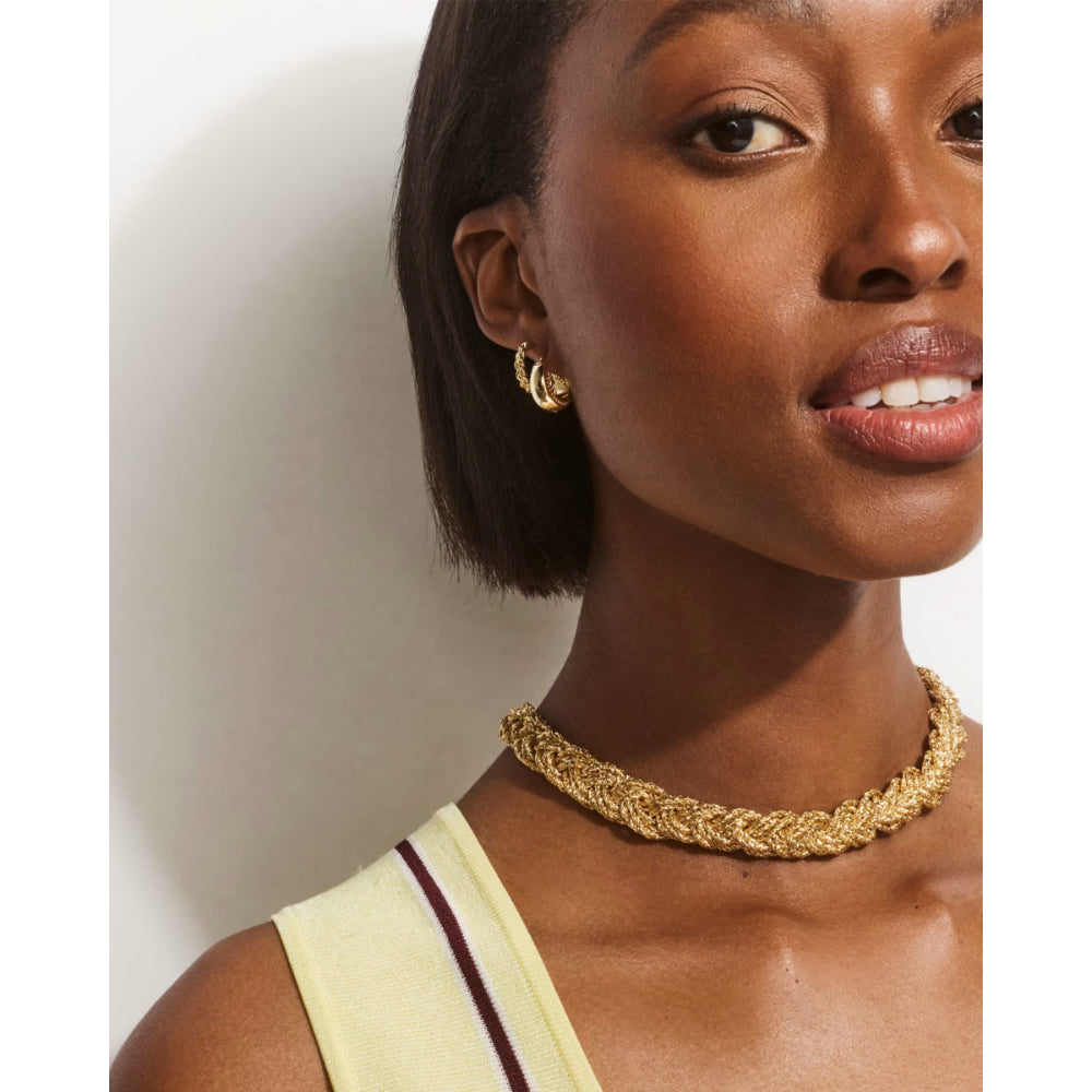 Woman wearing a gold braided necklace against a plain background