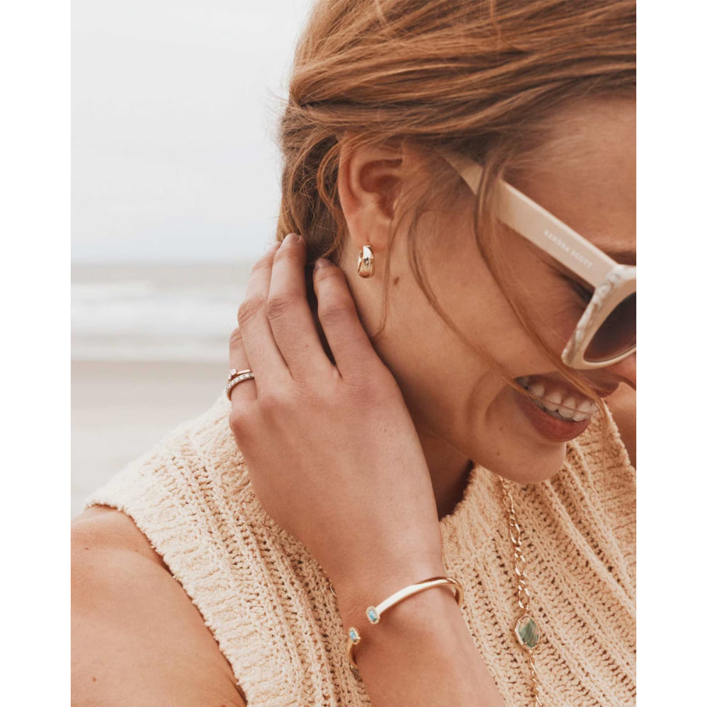 Woman wearing gold earrings, ring, and bracelet with a blurred background