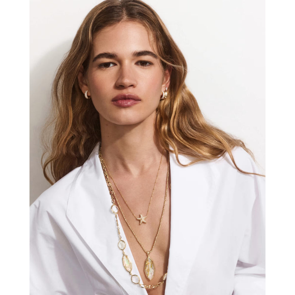 Woman wearing a white blazer and gold jewelry against a plain background