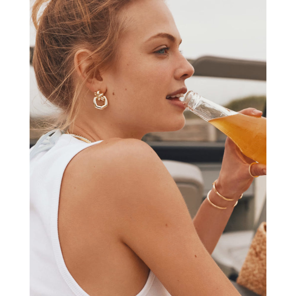 Woman drinking from a glass bottle with a yellow liquid outdoors