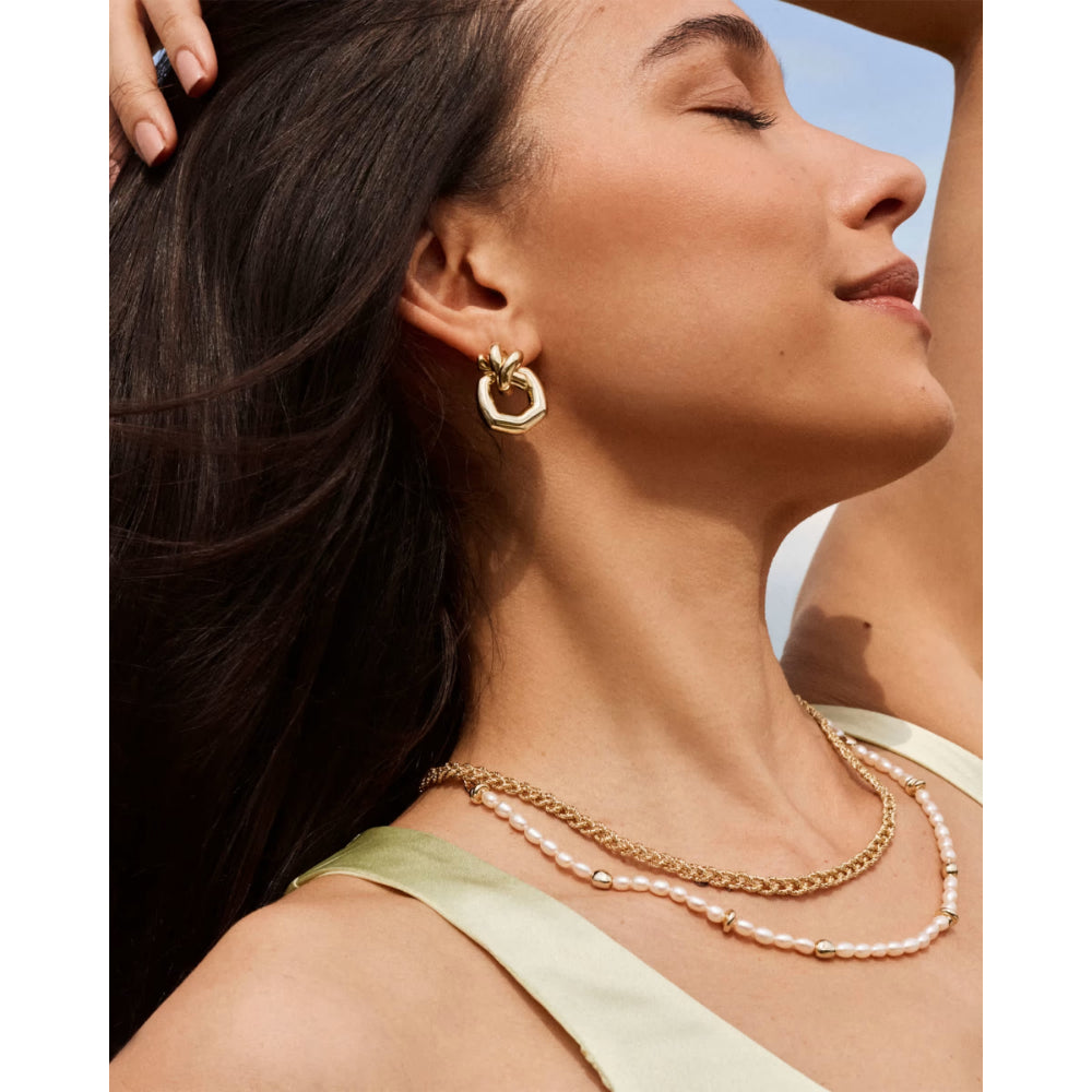 Woman wearing gold hoop earrings and pearl necklaces with a blurred background