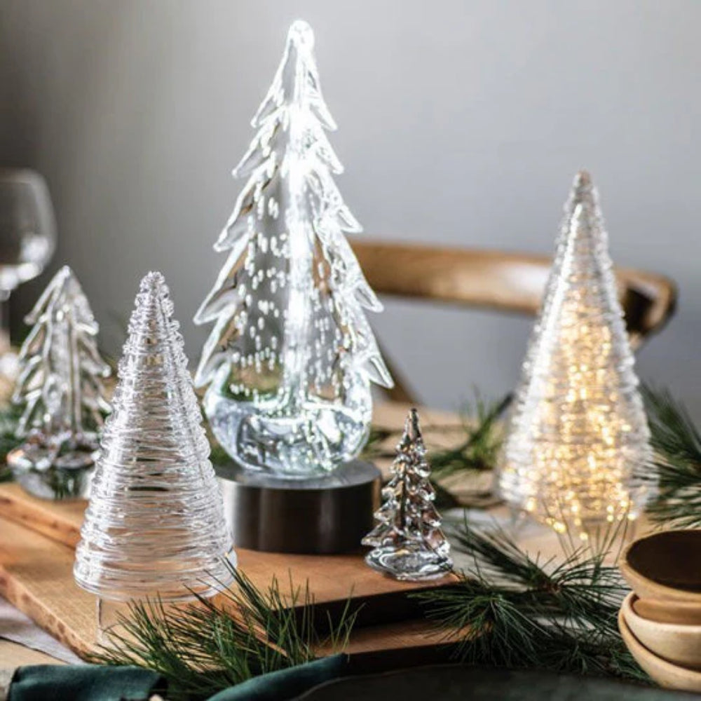 Clear glass evergreen trees on small and large LED illumination bases with a flat base and a central LED light, in a silver finish on a table holiday decor
