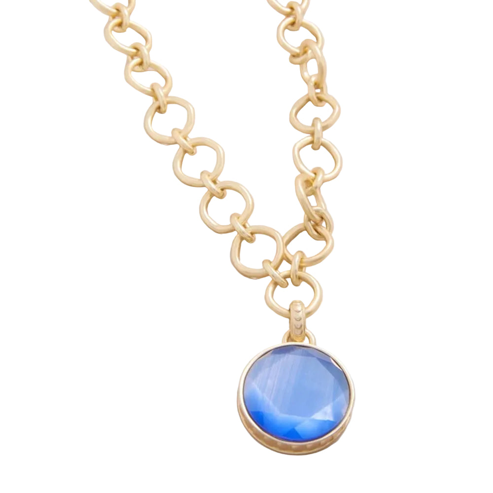 A gold chain necklace with a round blue faceted gemstone pendant in a gold bezel setting, shown on a light off-white background.