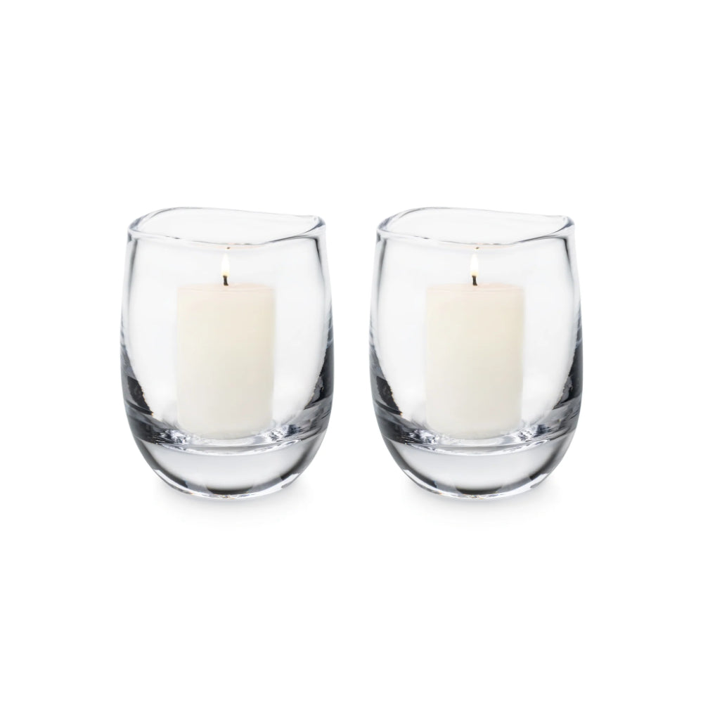 Two clear glass candle holders with white candles on a white background