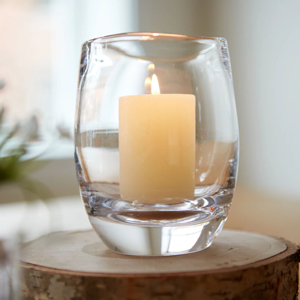 A close up photo of a candle in a clear glass holder on a wooden surface with a blurred background
