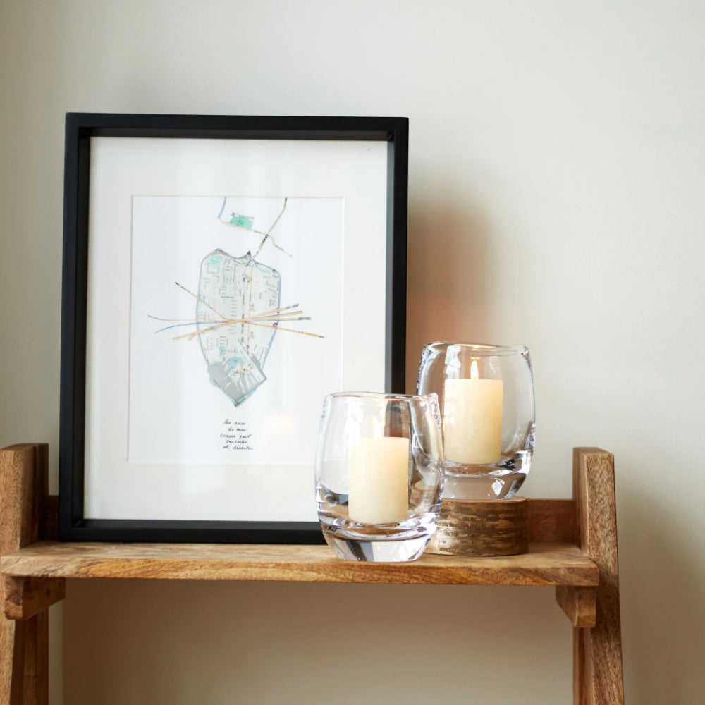 Framed artwork on a wooden shelf with candles in glass holders.