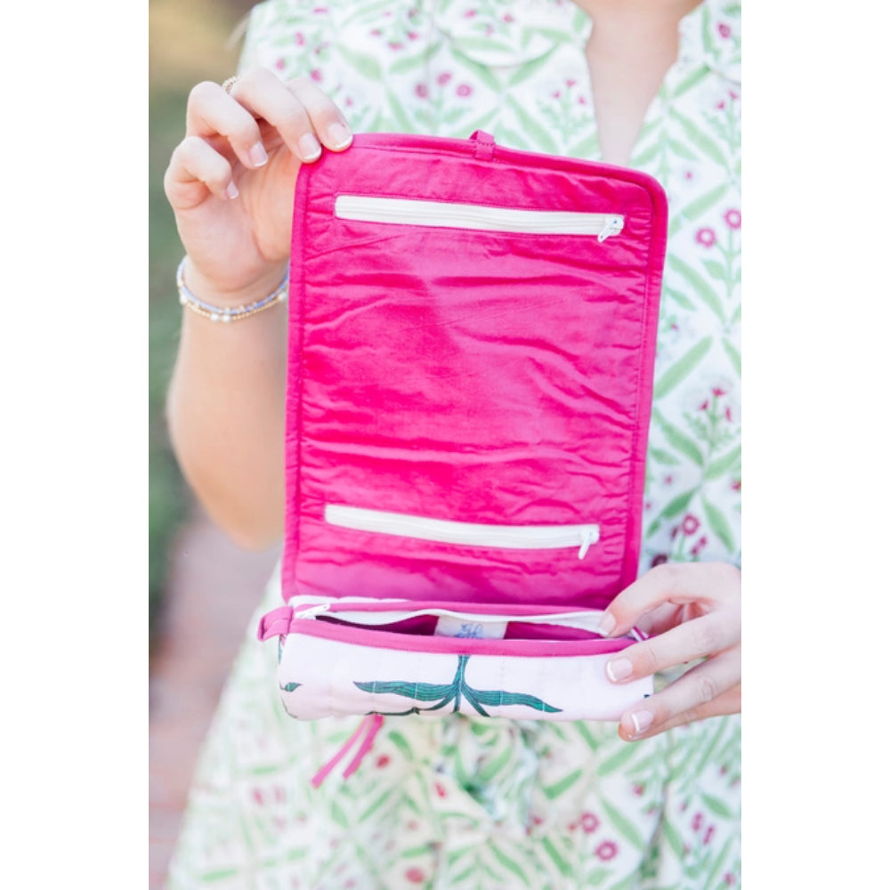 Pink travel jewelry roll held by a person wearing floral attire with a blurred background
