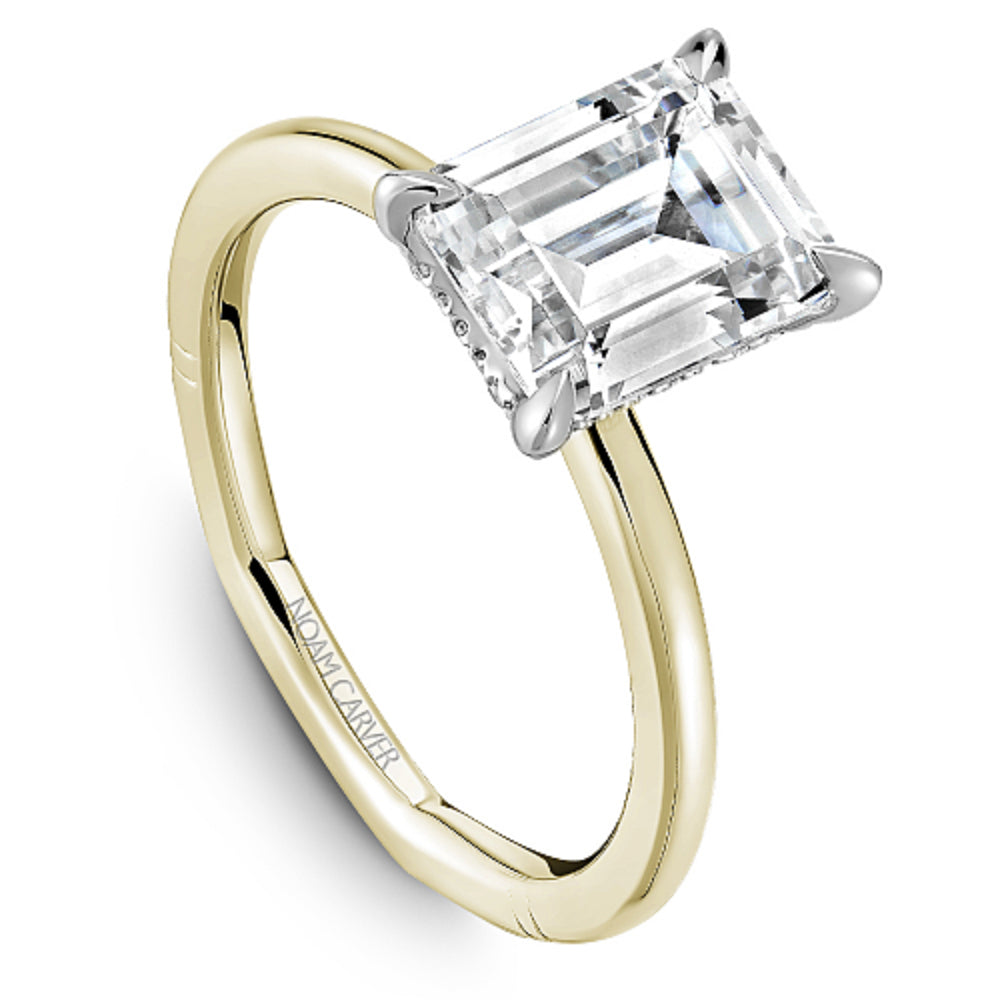 Gold Noam Carver ring with an emerald diamond center on a white background