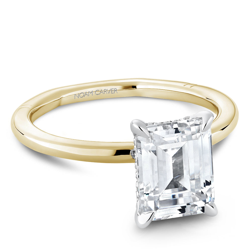 Gold Noam Carver ring with an emerald diamond center on a white background