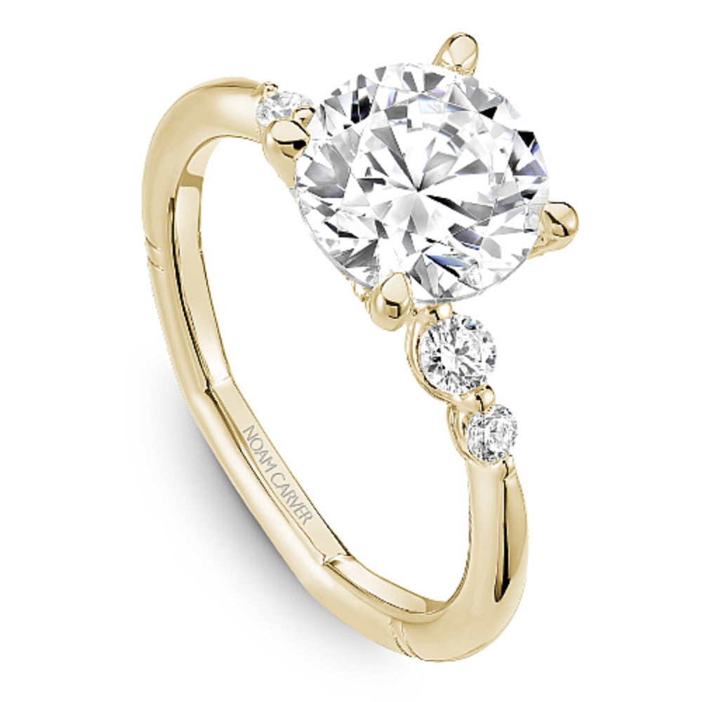 Gold Noam Carver ring with a large round diamond and smaller diamonds on the band against a white background