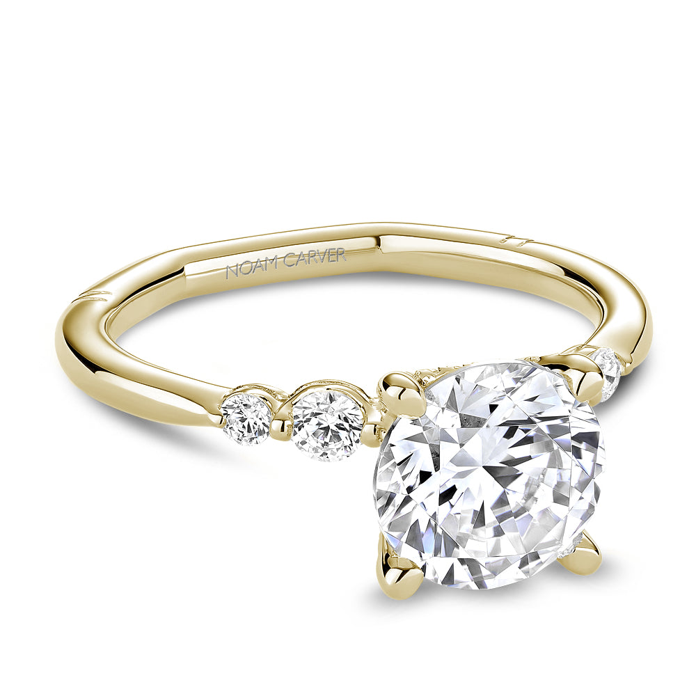 Gold Noam Carver ring with a large round diamond and smaller diamonds on the band against a white background