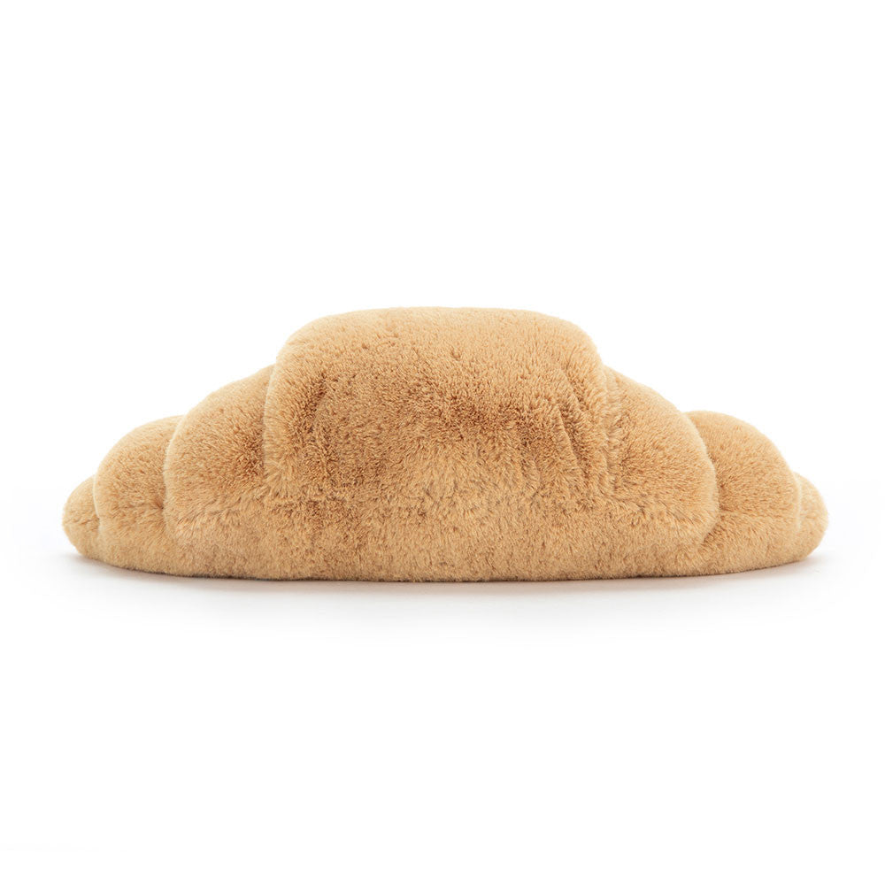 A photo of the back of a medium sized plush toy resembling a croissant with a happy facial expression and chocolate colored boots on a white backround.