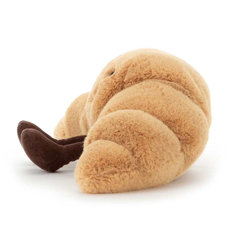 A side photo of a medium sized plush toy resembling a croissant with a happy facial expression and chocolate colored boots on a white backround.